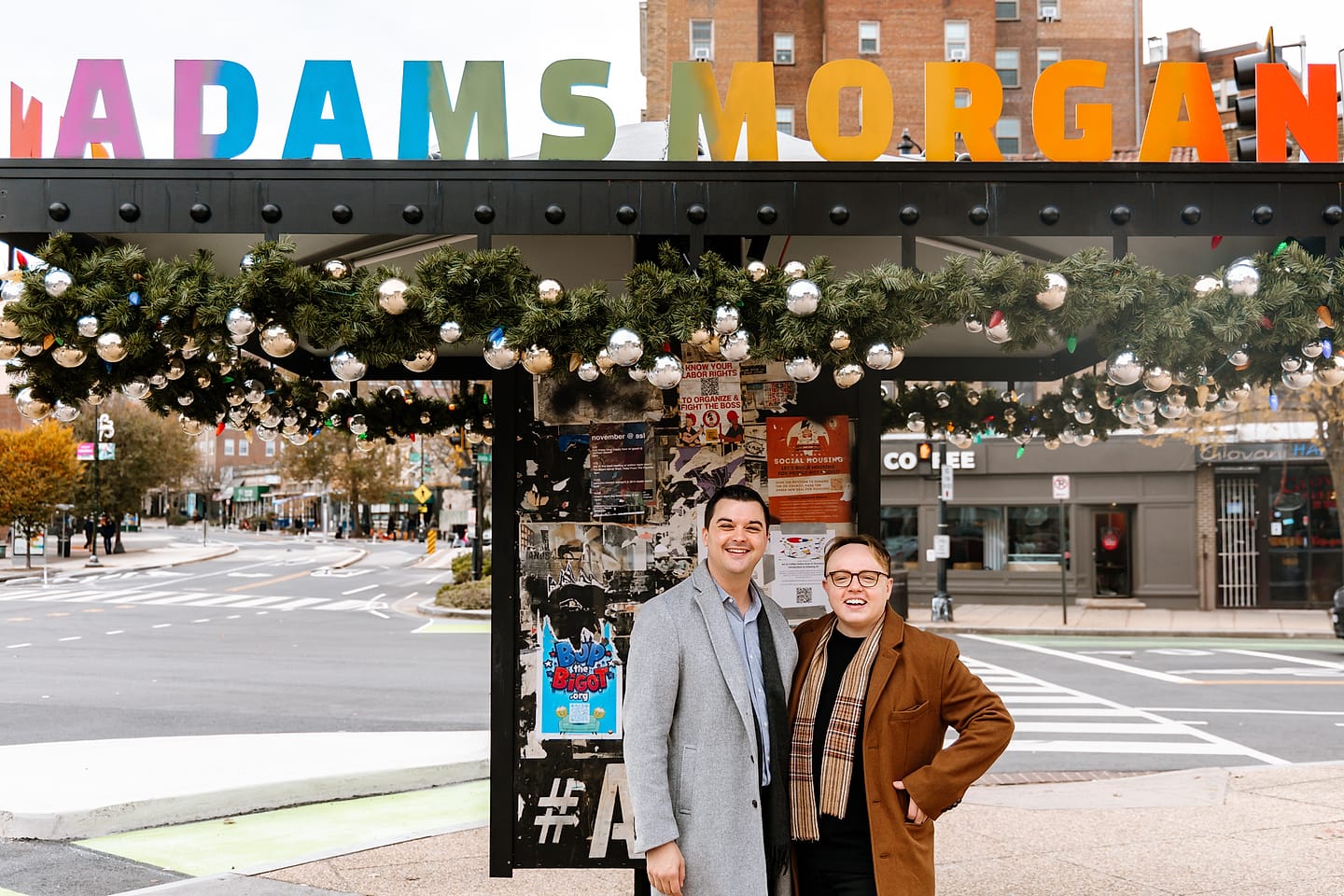Eric and JJ standing arm in arm beneath the colorful Adams Morgan sign during their Washington, DC engagement session