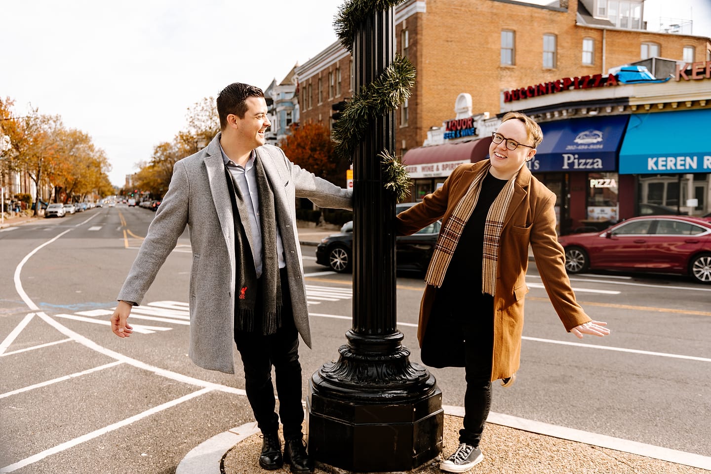 Eric and JJ laughing on either side of a lamppost near Duccini’s Pizza during their Adams Morgan engagement session in DC