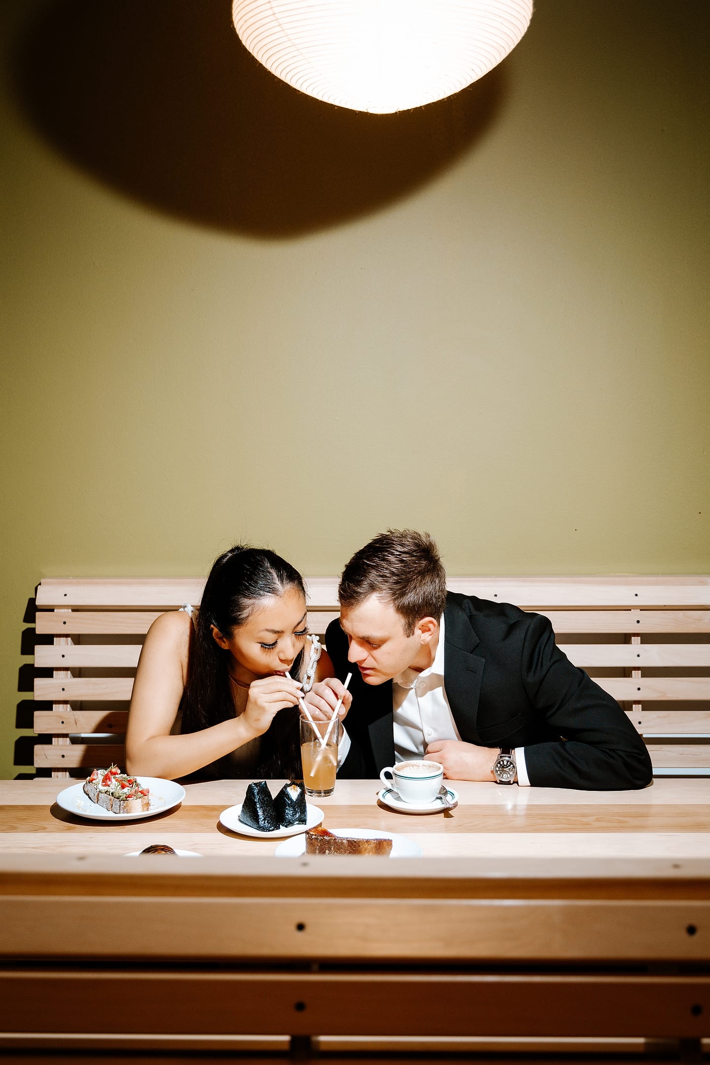 Jasmine and Aaron leaning in to sip drinks over a spread of food at Tonari during their Chinatown DC engagement session
