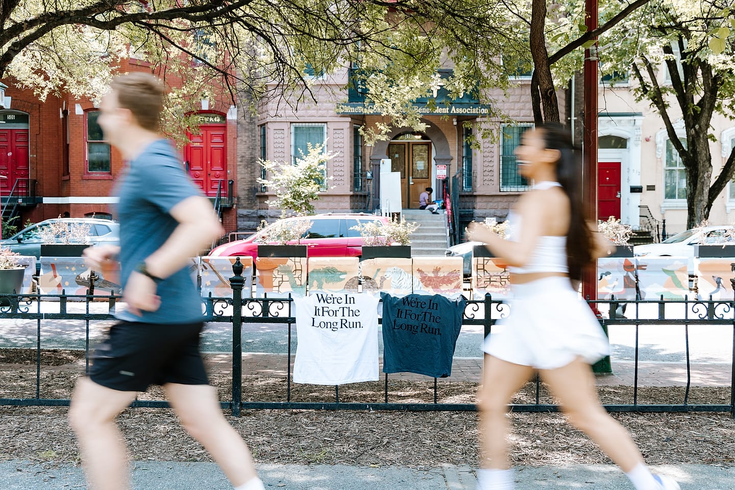 Runners pass a Chinatown mural fence hung with matching ‘We’re In It For The Long Run’ shirts in Washington, DC
