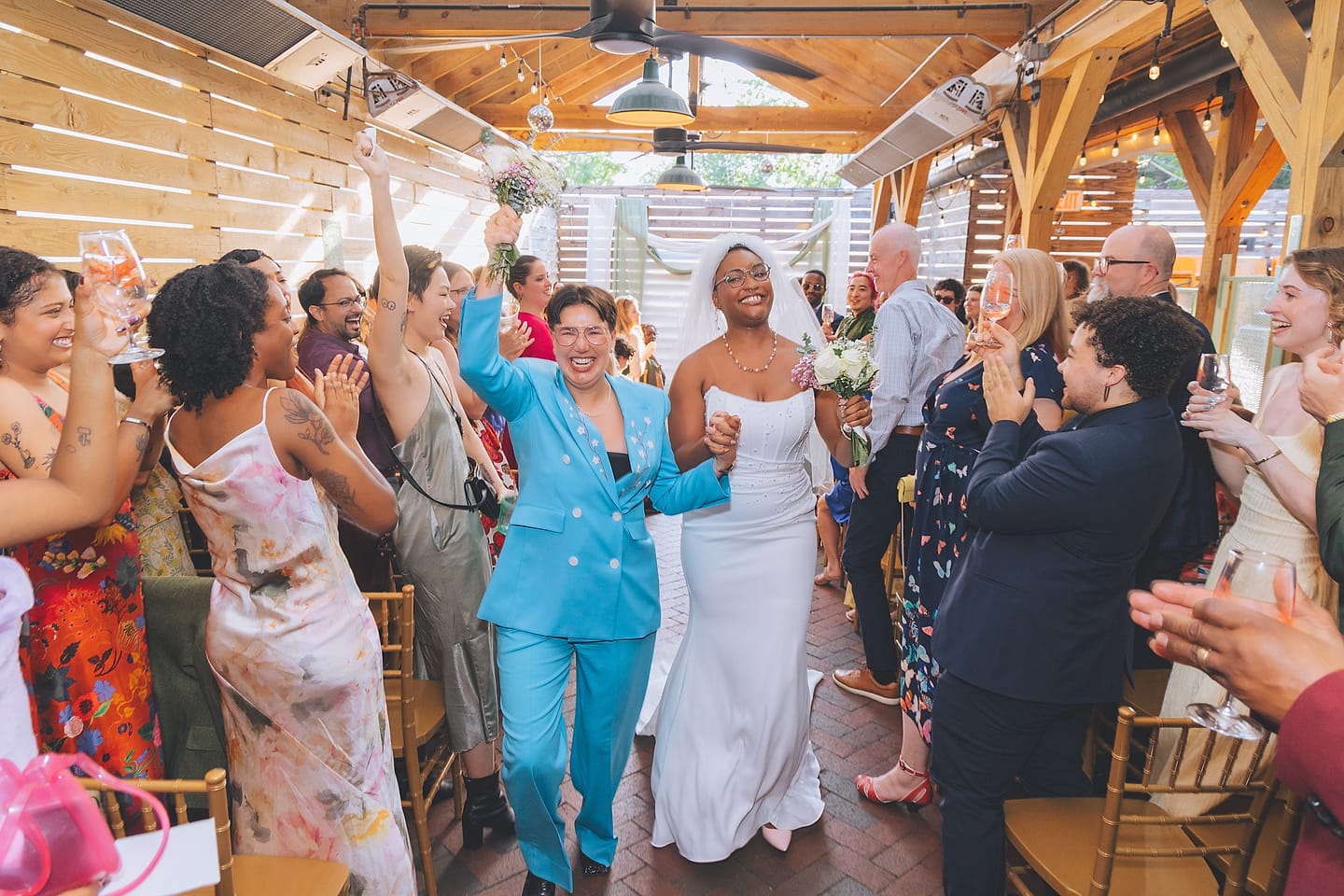 Two brides enter to cheering guests under a wooden pavilion at their DC wedding