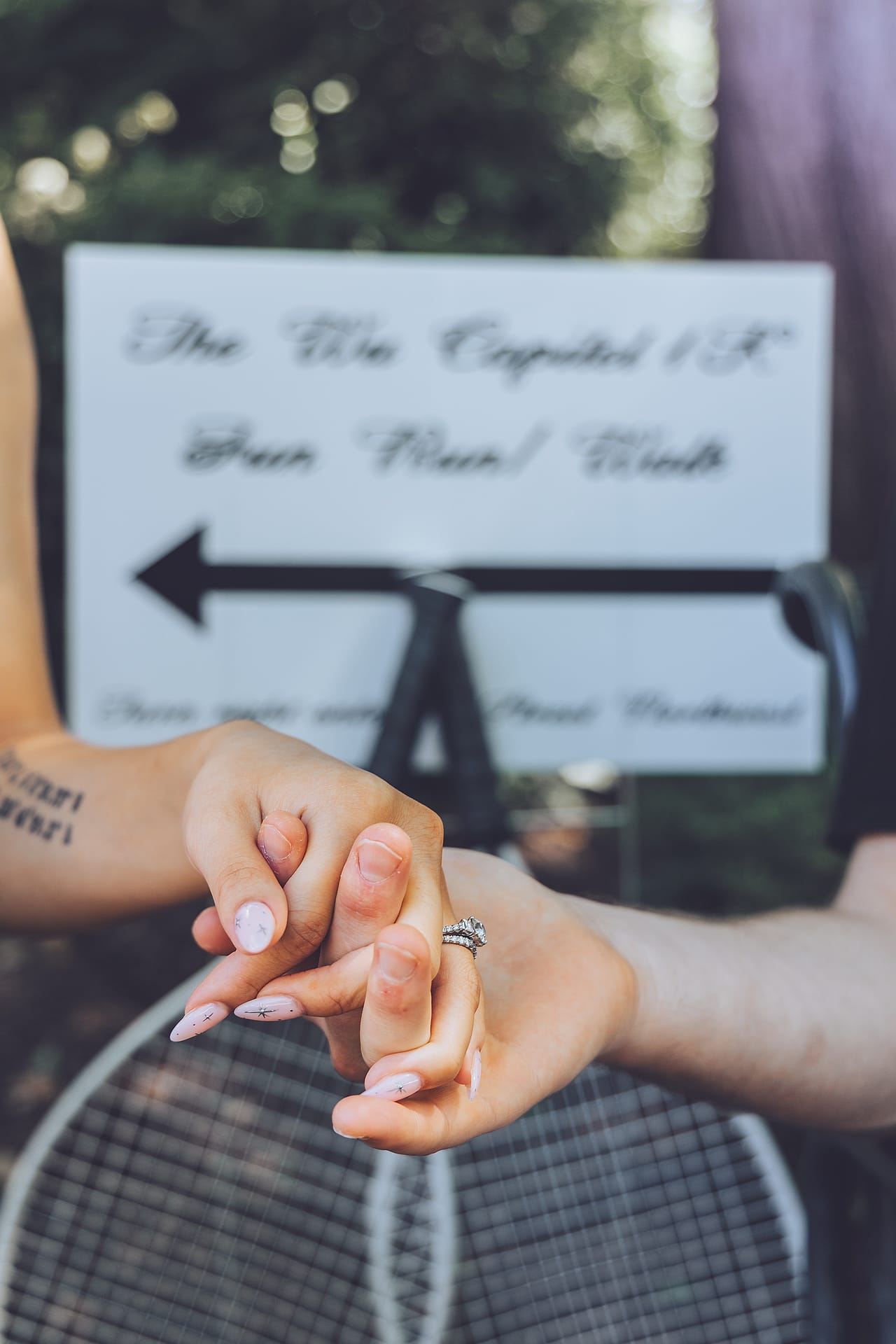 Couple links hands showing their wedding rings beside a playful wedding-weekend fun run sign