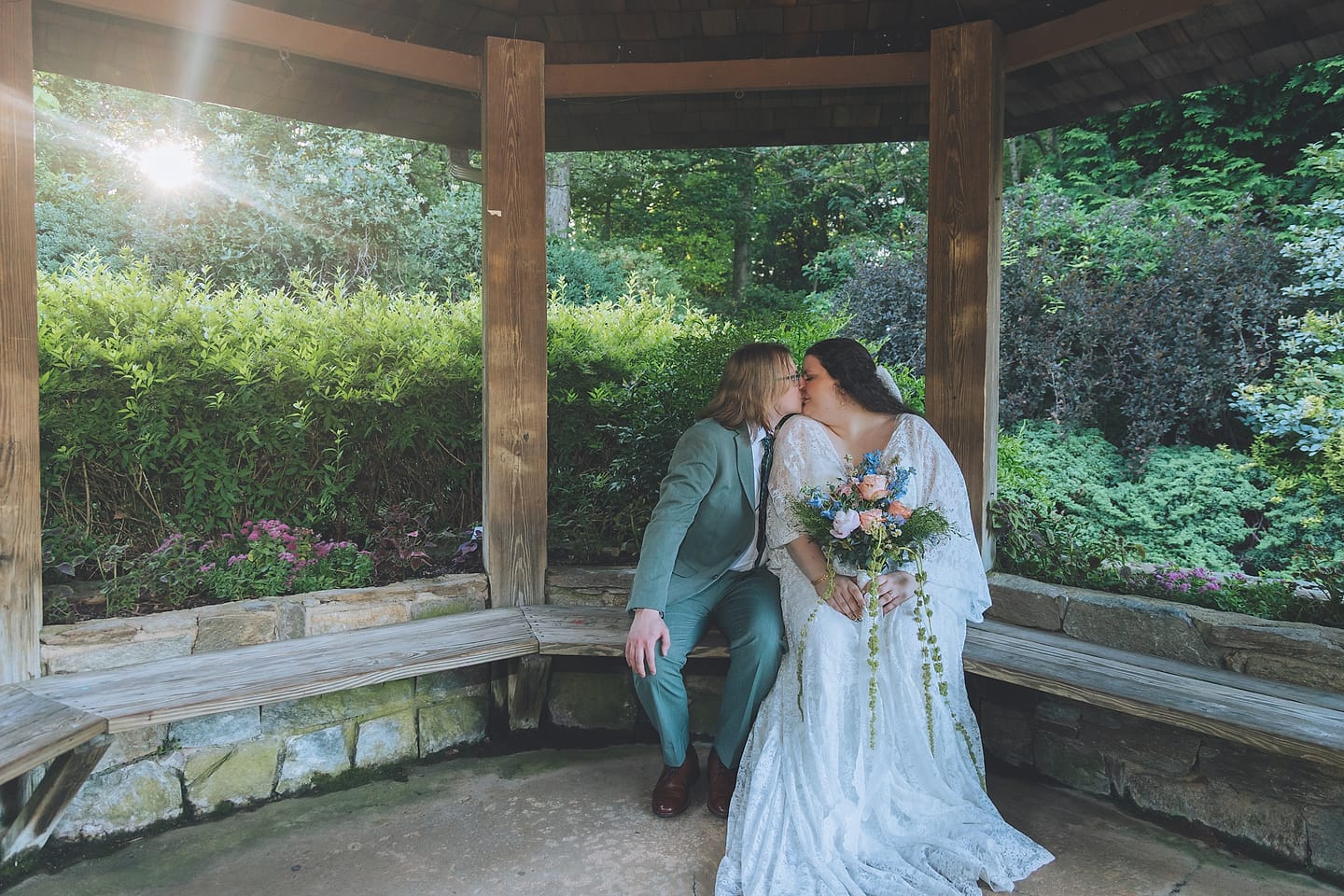 Couple kisses on a stone bench inside a garden gazebo at their Brookside Gardens wedding