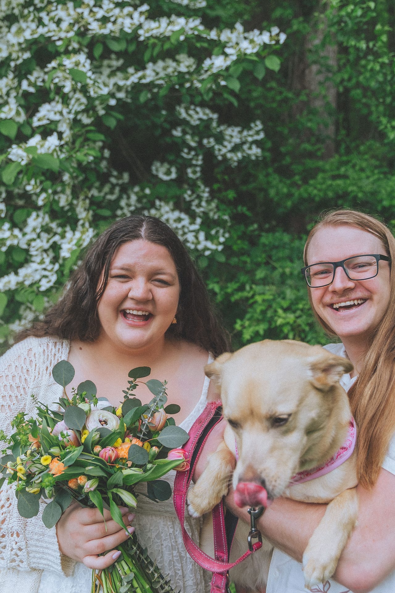 Todd and Olivia laugh together holding a wildflower bouquet and their dog at their DMV garden wedding