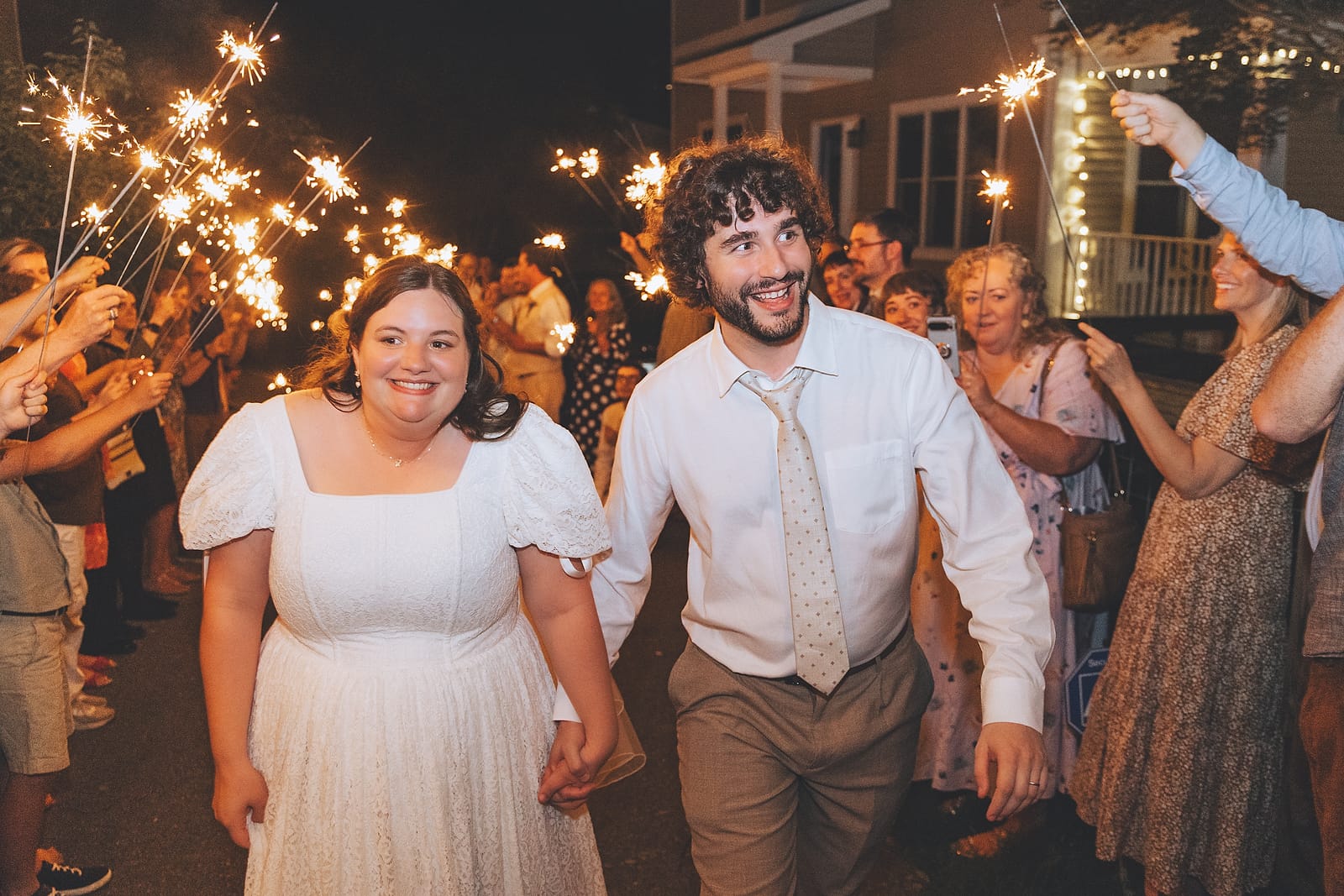 Newlyweds smiling as they walk through a glowing sparkler exit