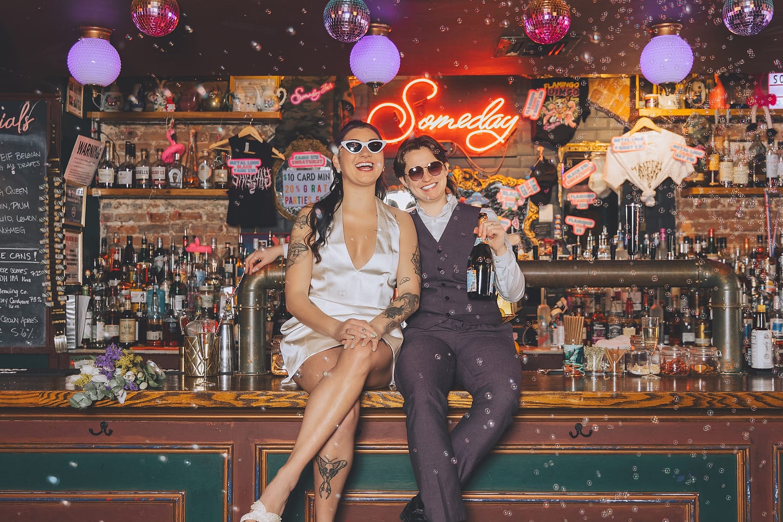 Two newlyweds laughing together at the Someday bar beneath disco balls